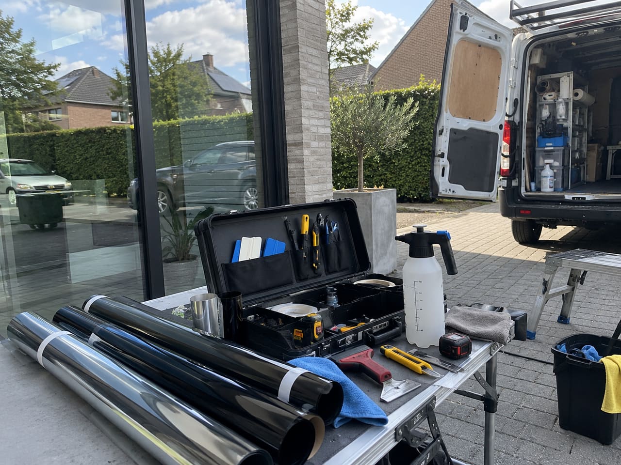 Folierollen, rakels en ander gereedschap op een werktafel naast een raam.